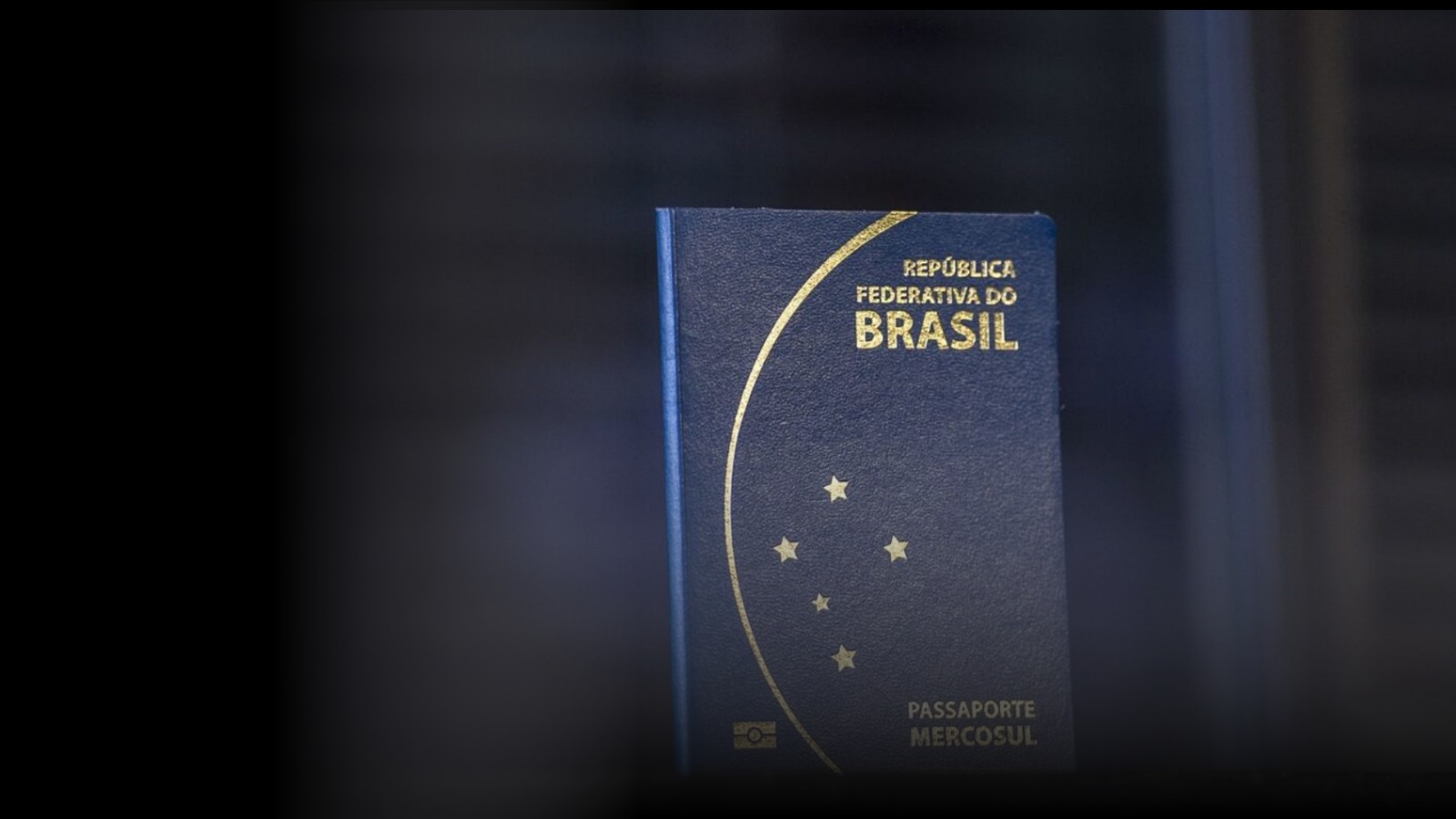 Capa azul do Passaporte Brasileiro com detalhes dourados, em fundo escuro